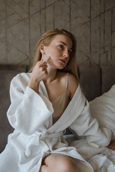 Woman in bathrobe using gua sha for a relaxing morning skincare ritual.