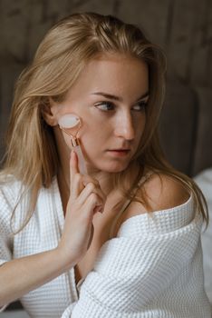 Young woman using a rose quartz face roller in a skincare routine. Indoor self-care concept.