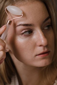 Close-up of a woman using a jade roller for anti-aging skincare treatment indoors.