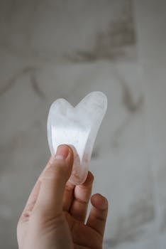 Close-up of a hand holding a jade gua sha tool against an elegant marble backdrop. Perfect for wellness and beauty themes.