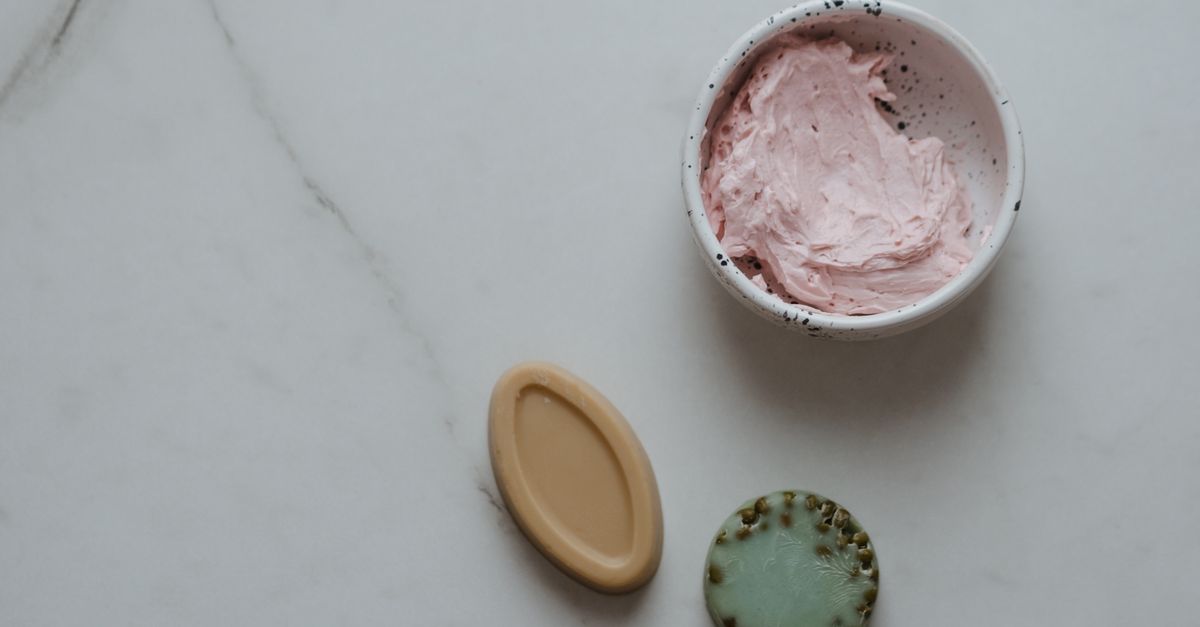 Top view of natural skincare products including soaps and cream on a marble background.
