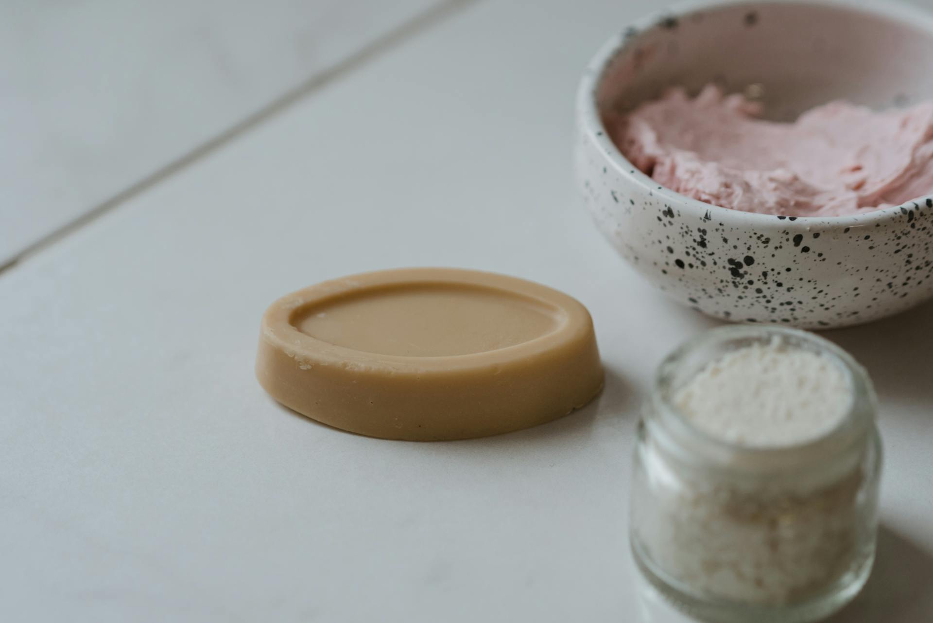 A close-up of natural skincare products on a marble surface, featuring soap and scrub.