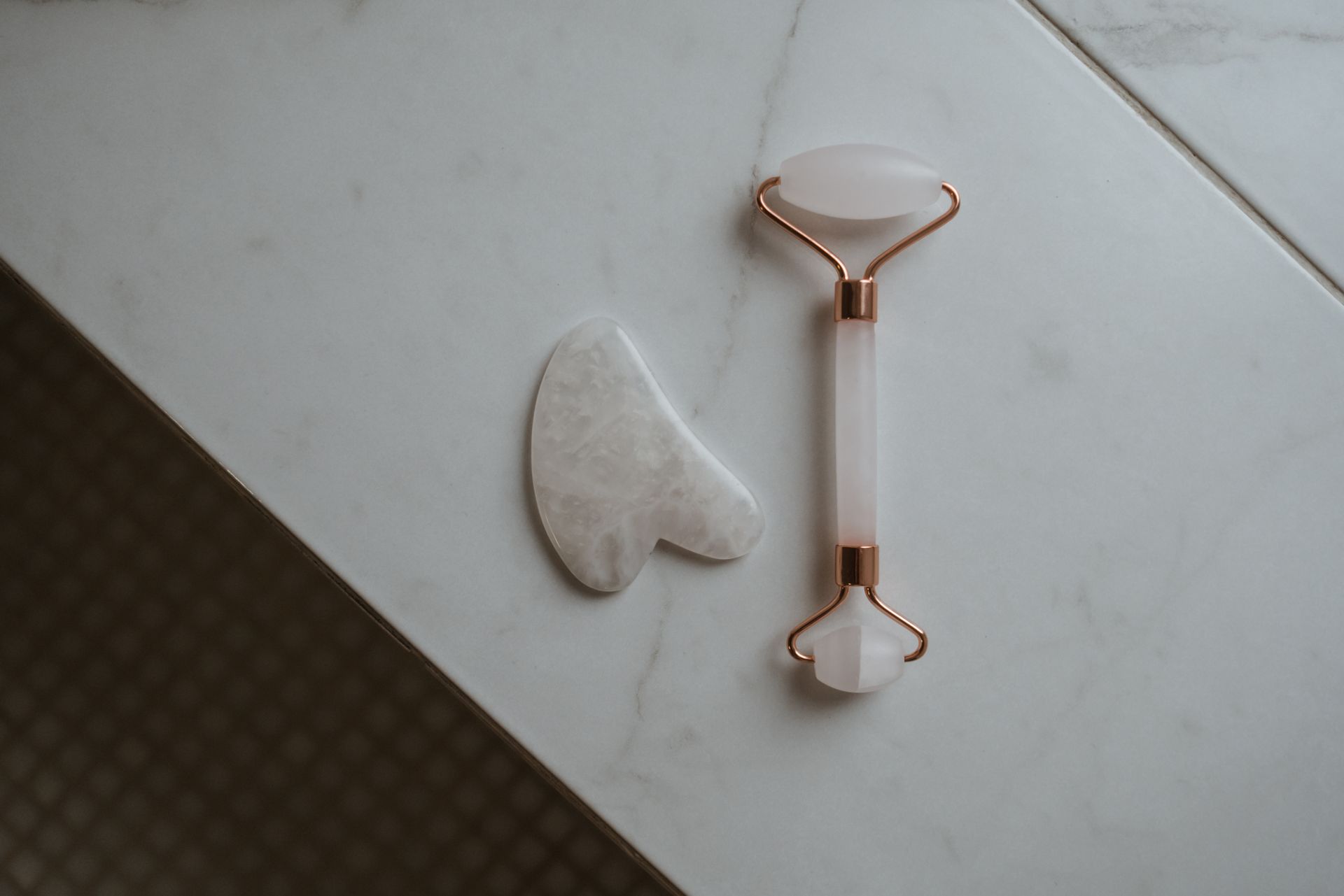 Elegant top view of a jade gua sha tool and facial roller on a marble background for skincare routines.