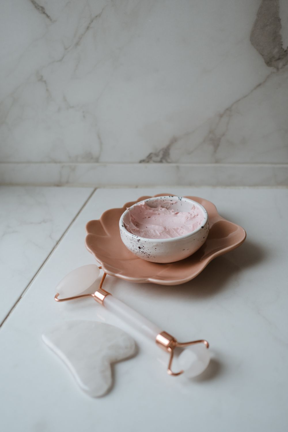A stone gua sha tool, a steel ice roller and a wooden dry brush laid on linen, each carrying a small engraved mark