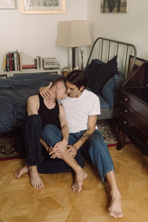 Free Gay Couple Sitting on the Floor by the Bed and Hugging  Stock Photo