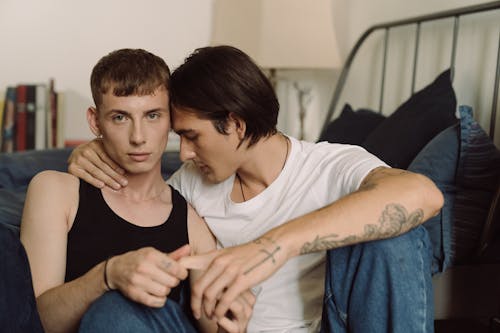 Free Gay Couple Sitting on the Floor by the Bed and Hugging  Stock Photo