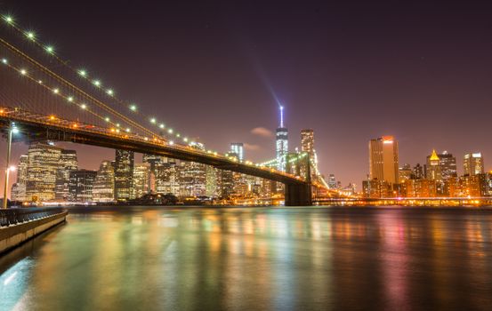 夜晚，标志性的布鲁克林大桥和纽约市天际线在平静的水面上闪闪发光
