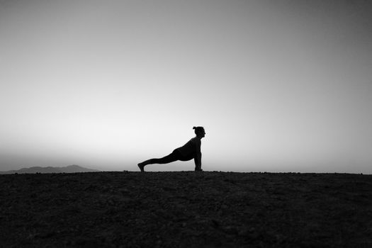 A serene silhouette of a woman in a yoga pose outdoors at sunset, creating a peaceful ambiance.
