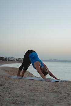 A woman performing yoga on a beach at sunset, embodying fitness and tranquility.