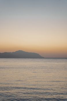 日落时分，平静的海水映照着色彩缤纷的天空，远处山峰的轮廓依稀可见