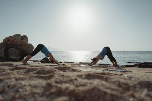 Two women practicing yoga at dawn on a serene beach with clear waters.