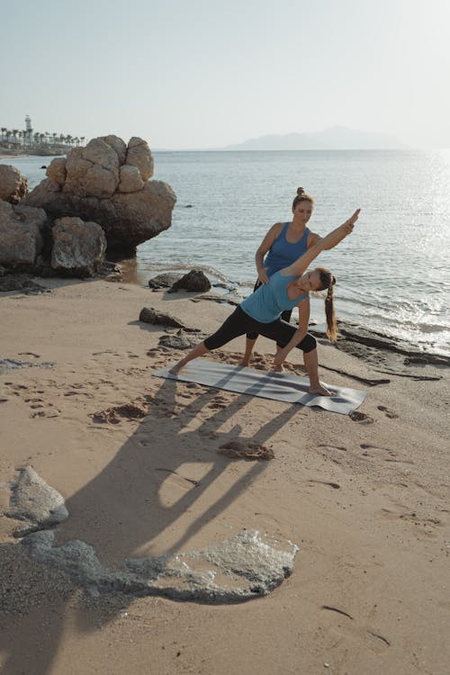 Woman in Blue Tank Top and Black Pants Sitting on Brown Wooden Seat on Beach during