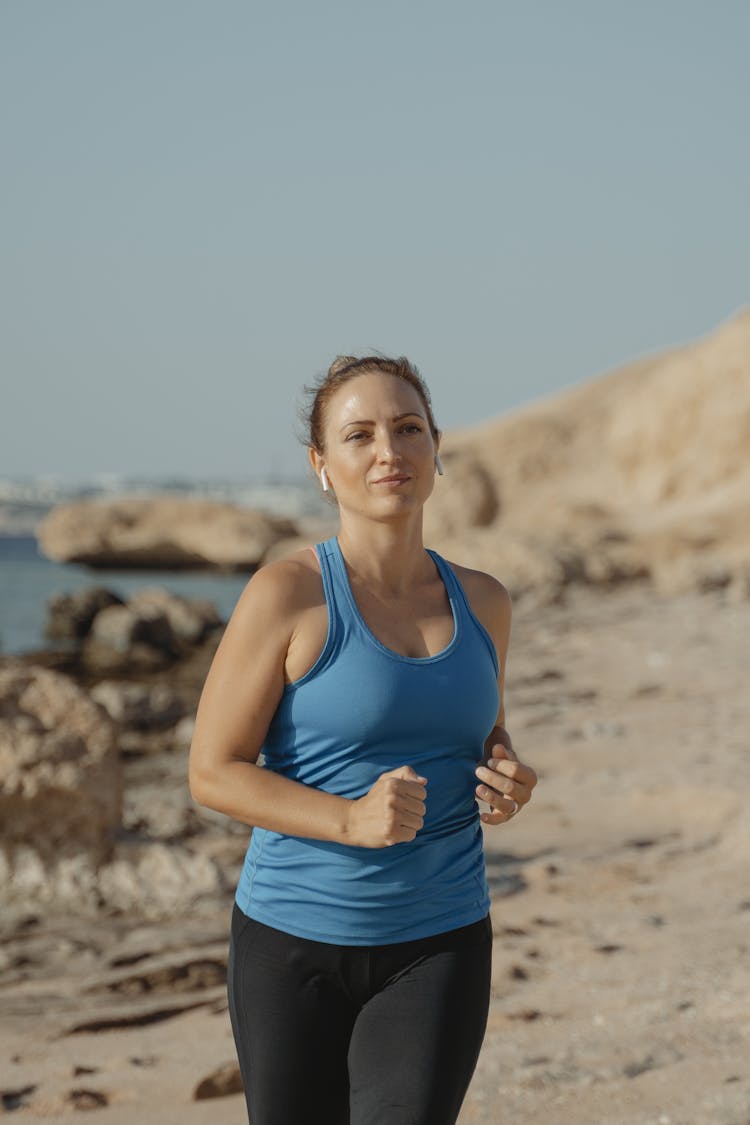 A Woman In Blue Tank Top Running On The Beach