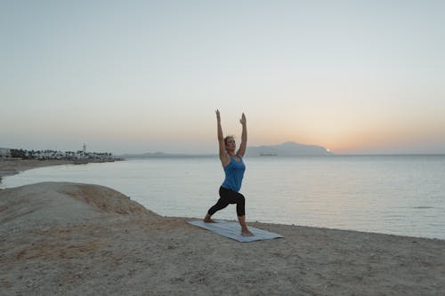 A Woman in Warrior 1 Pose at the Beach During Twilight