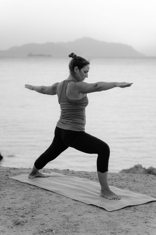 Free Caucasian woman doing yoga on a beach, demonstrating balance and focus in grayscale. Stock Photo