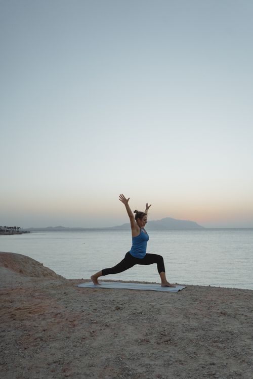 Free Woman performing yoga on a beach at sunrise, embracing balance and tranquility. Stock Photo
