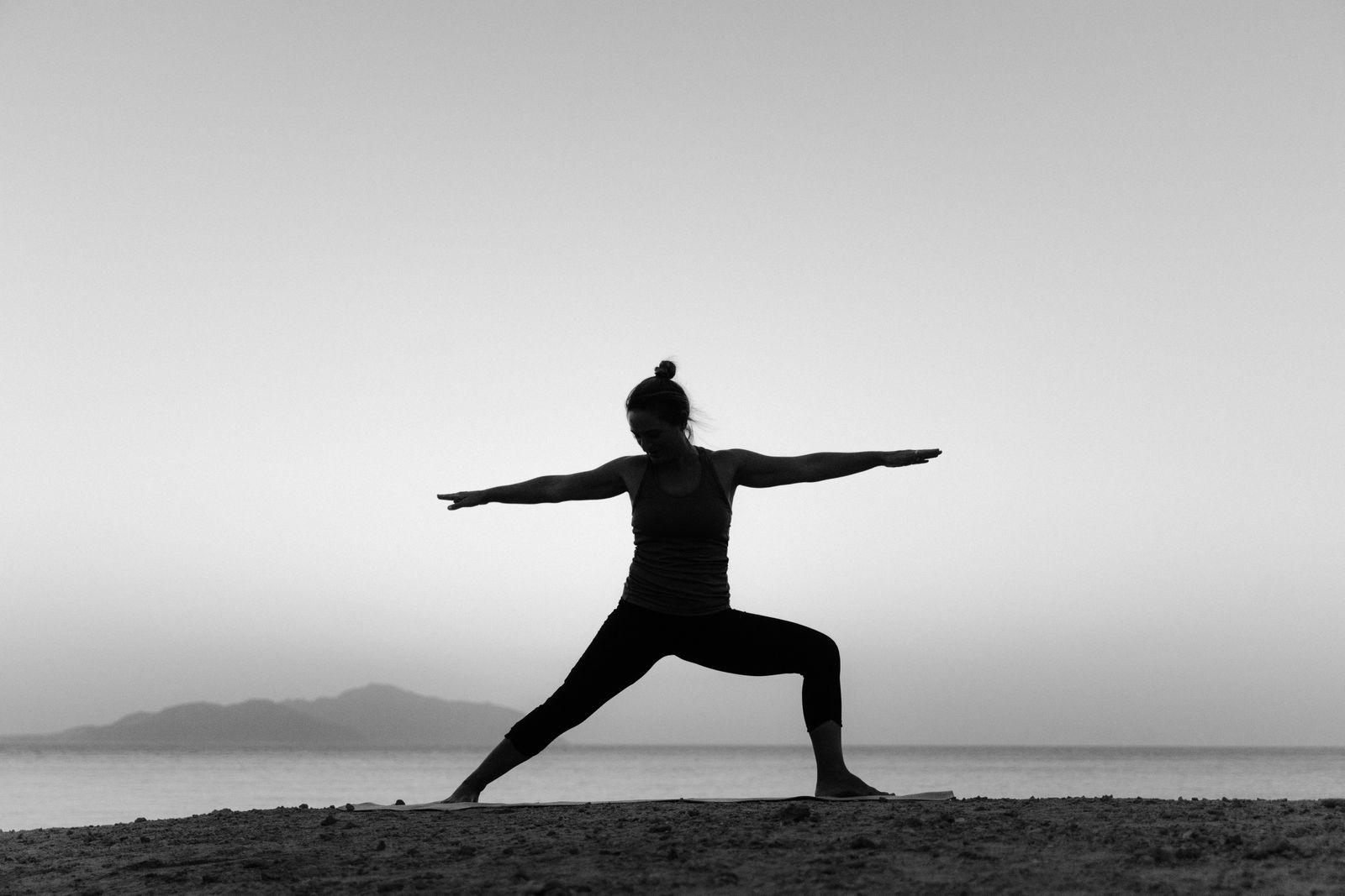Silhouette of a woman practicing Virabhadrasana warrior pose on a beach at sunset