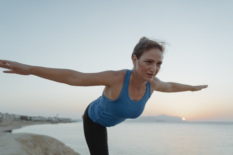 Woman Practising Yoga On The Shore At Sunrise