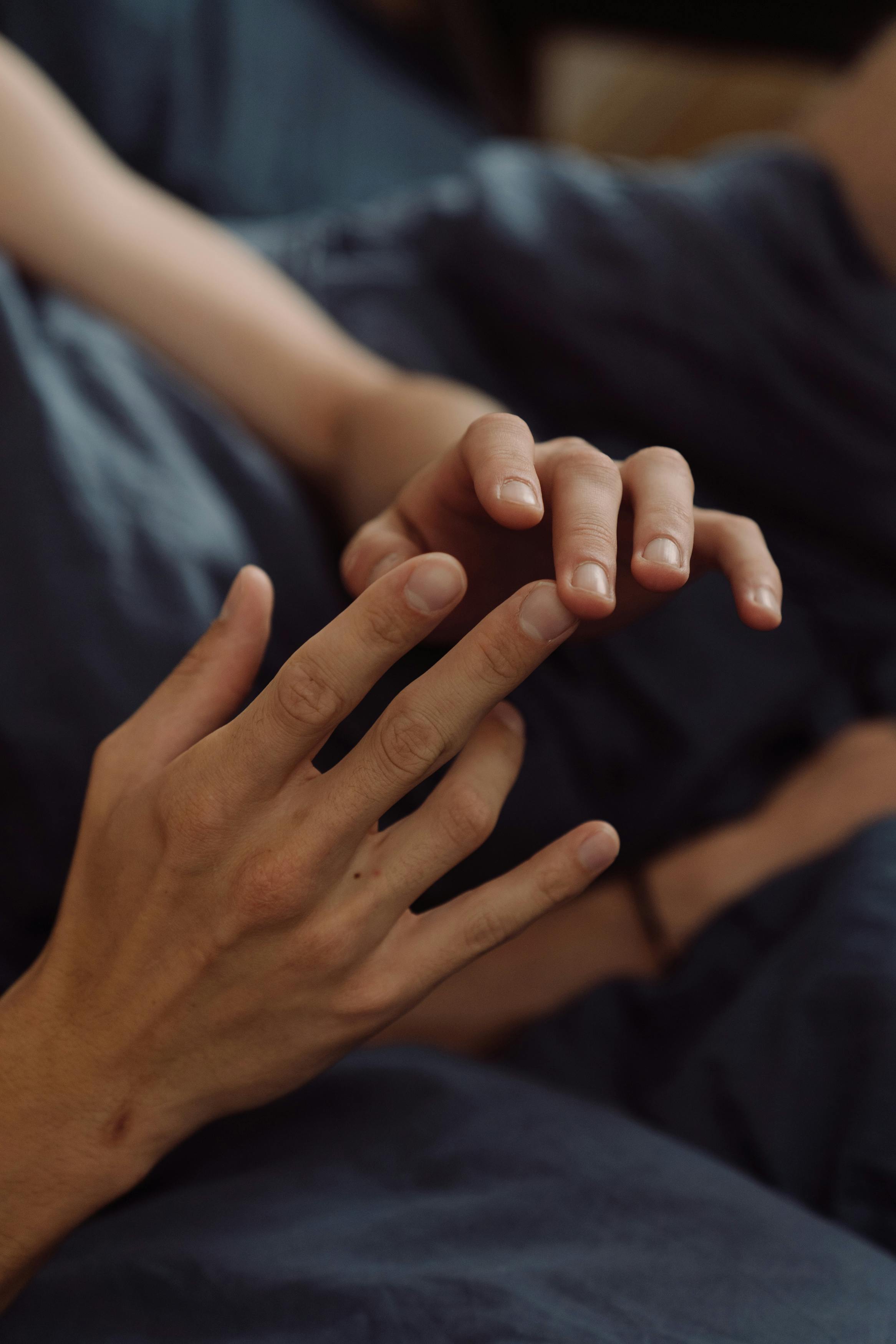 Close-up of lovers' hands gently touching on soft silk sheets, intimate and tender in dim bedroom light