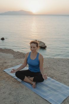 Woman meditating on a beach at sunset, promoting tranquility and mindfulness.