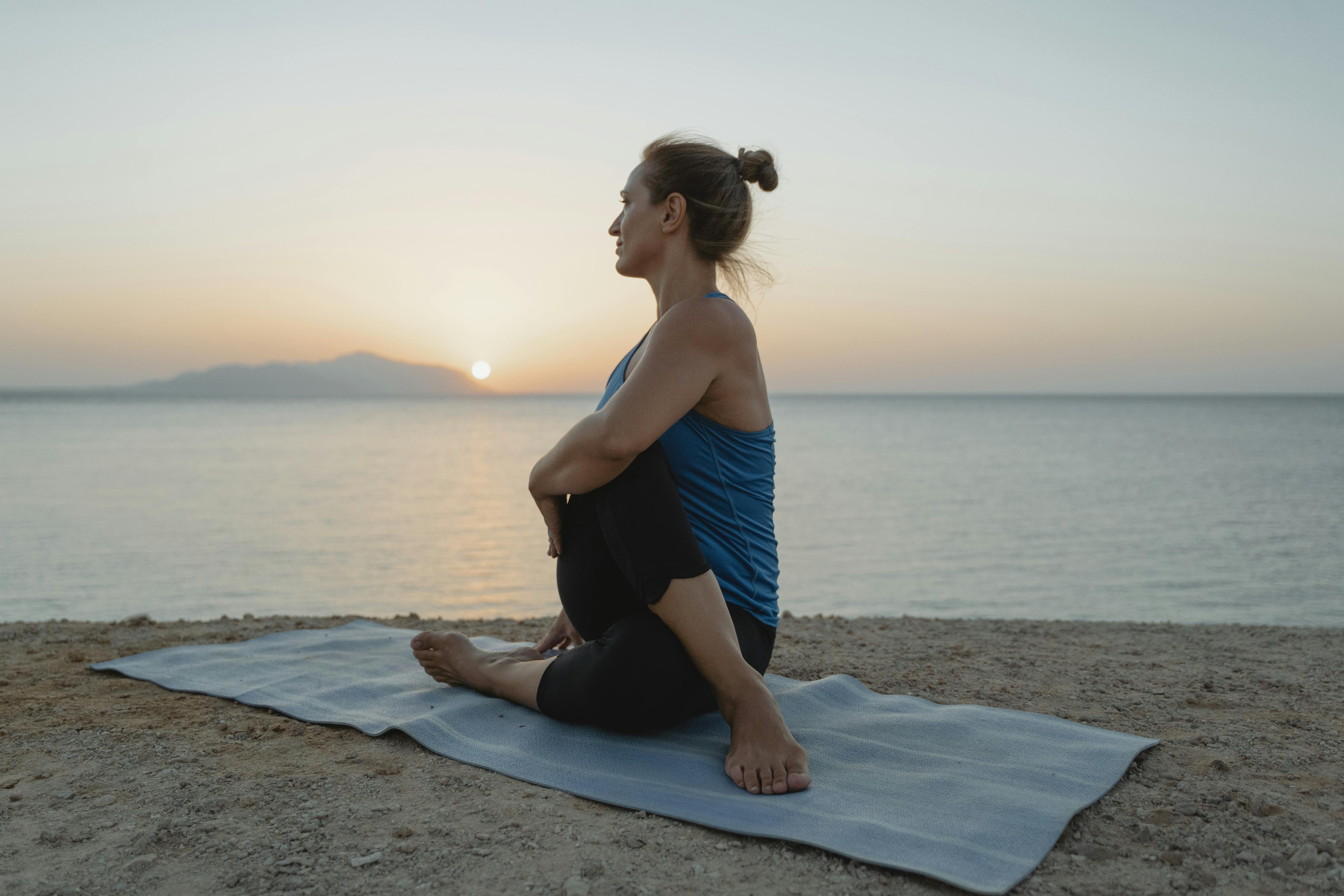 Serene scene of a woman doing yoga on the beach during a tranquil sunset.