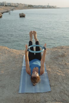 A woman doing yoga with a ring on a cliff overlooking the ocean during sunset.