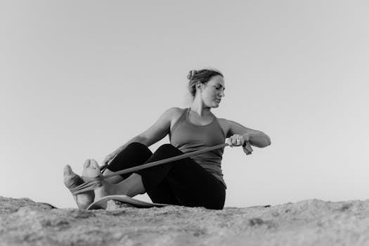A woman practicing yoga with a resistance band on a beach in black and white.