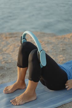 Woman doing yoga with a ring on a beach mat by the sea at sunset.