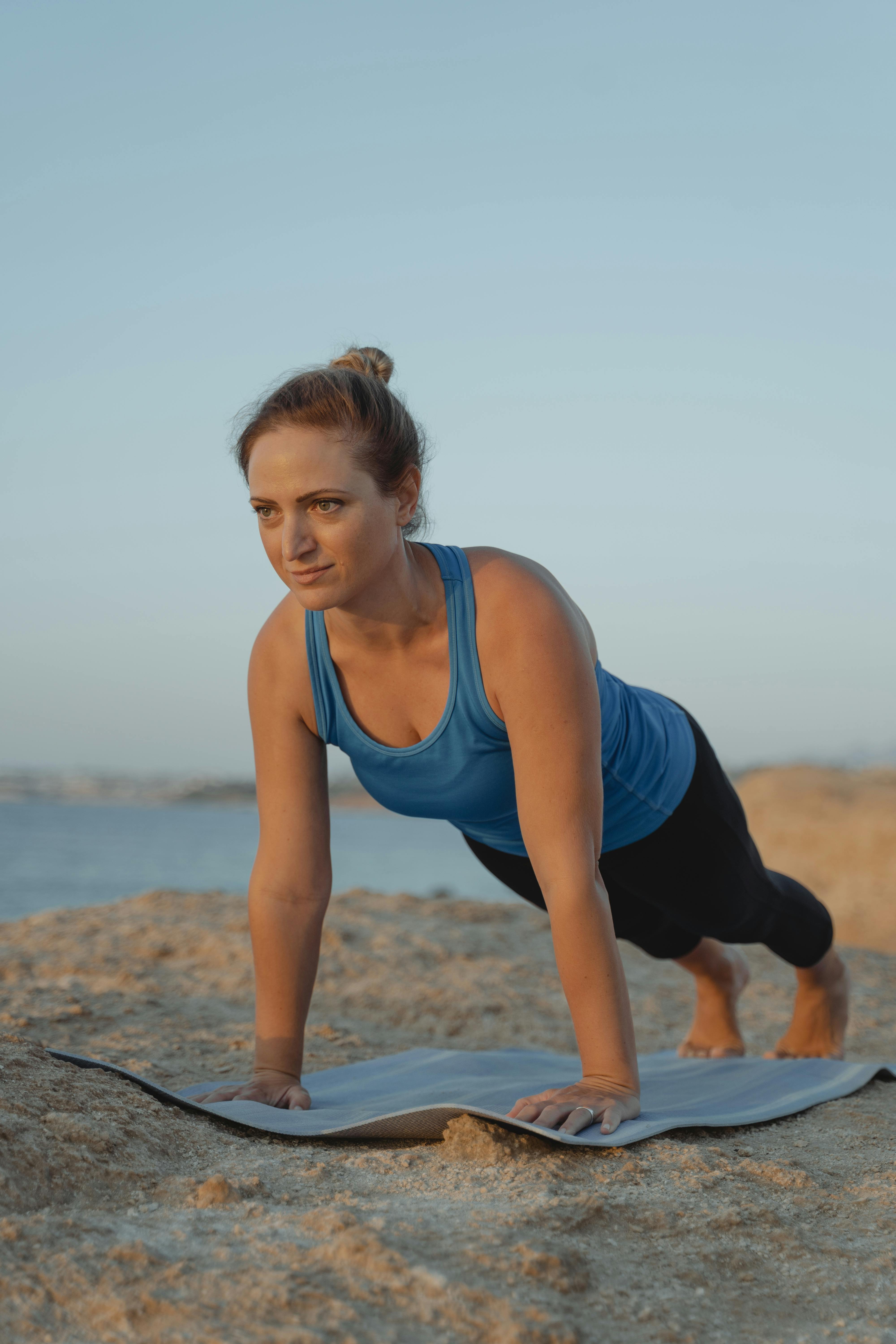 专注的女人白天在海滩上的瑜伽垫上练习木板姿势