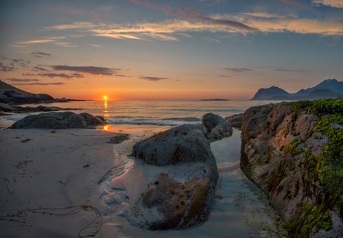Free A picturesque sunset over a rocky beach with a calm sea and distant mountains. Stock Photo