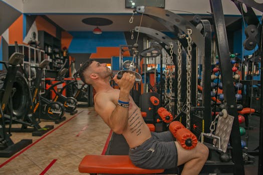 Tattooed man performs strength training on gym equipment, showcasing fitness.
