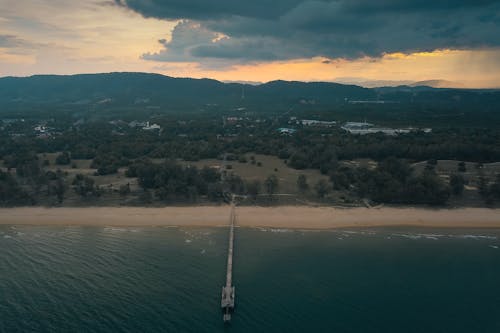 Ocean with pier against green ridges at sunset