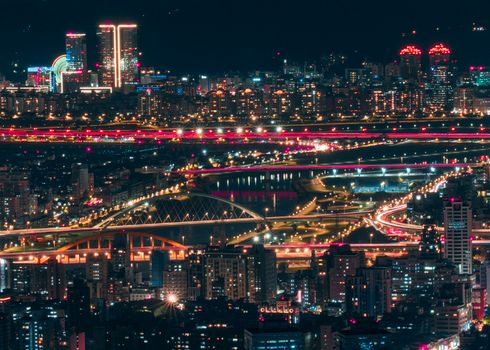Drone view of modern glowing city with skyscrapers and buildings with roads and bridges over river at night