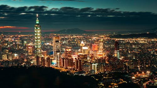Free Taipei city in Taiwan with modern glowing buildings and skyscrapers with Taipei 101 tower near hills at night under cloudy sky Stock Photo