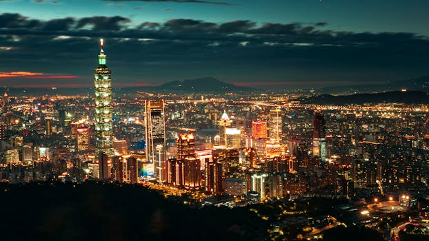 Taipei city in Taiwan with modern glowing buildings and skyscrapers with Taipei 101 tower near hills at night under cloudy sky