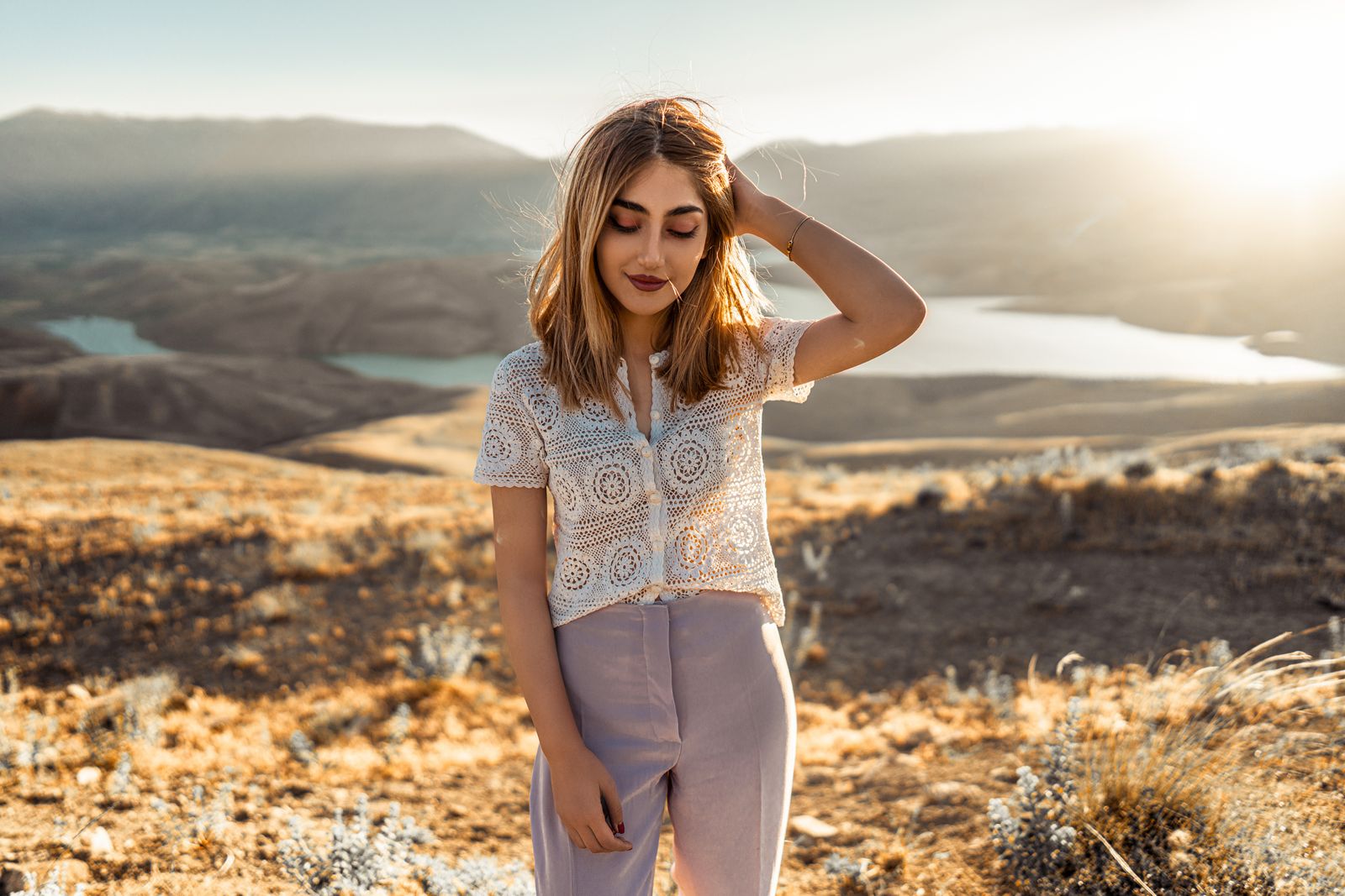 A young woman poses in a sunlit desert landscape, exuding tranquility and style.