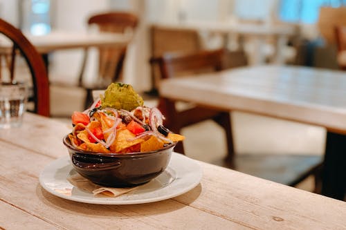Tasty fresh nachos with guacamole in bowl on wooden table in Mexican restaurant