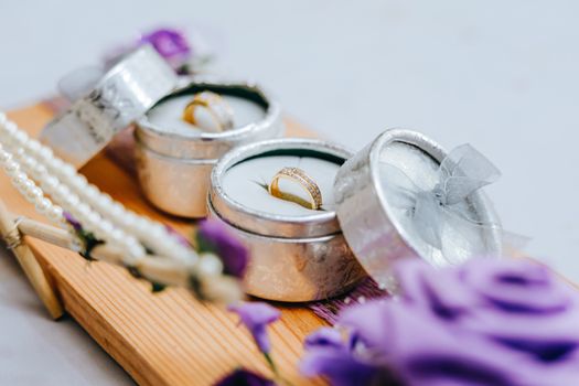 Golden wedding rings in small grey boxes on wooden stand with purple flowers