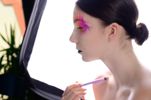 A unique side profile of a woman with colorful, expressive makeup and black lipstick.