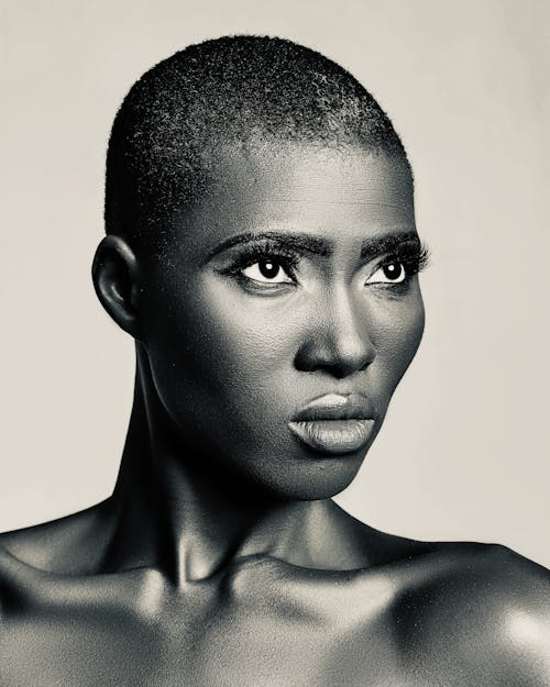 Black and white of African American female with short hair and bare shoulders standing against white background in studio and looking up