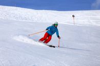 Person in Green Jacket and Blue Helmet Riding on Ski Blades on Snow Covered Ground during