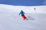 Person in Blue Jacket and Red Pants Riding Ski Blades on Snow Covered Ground