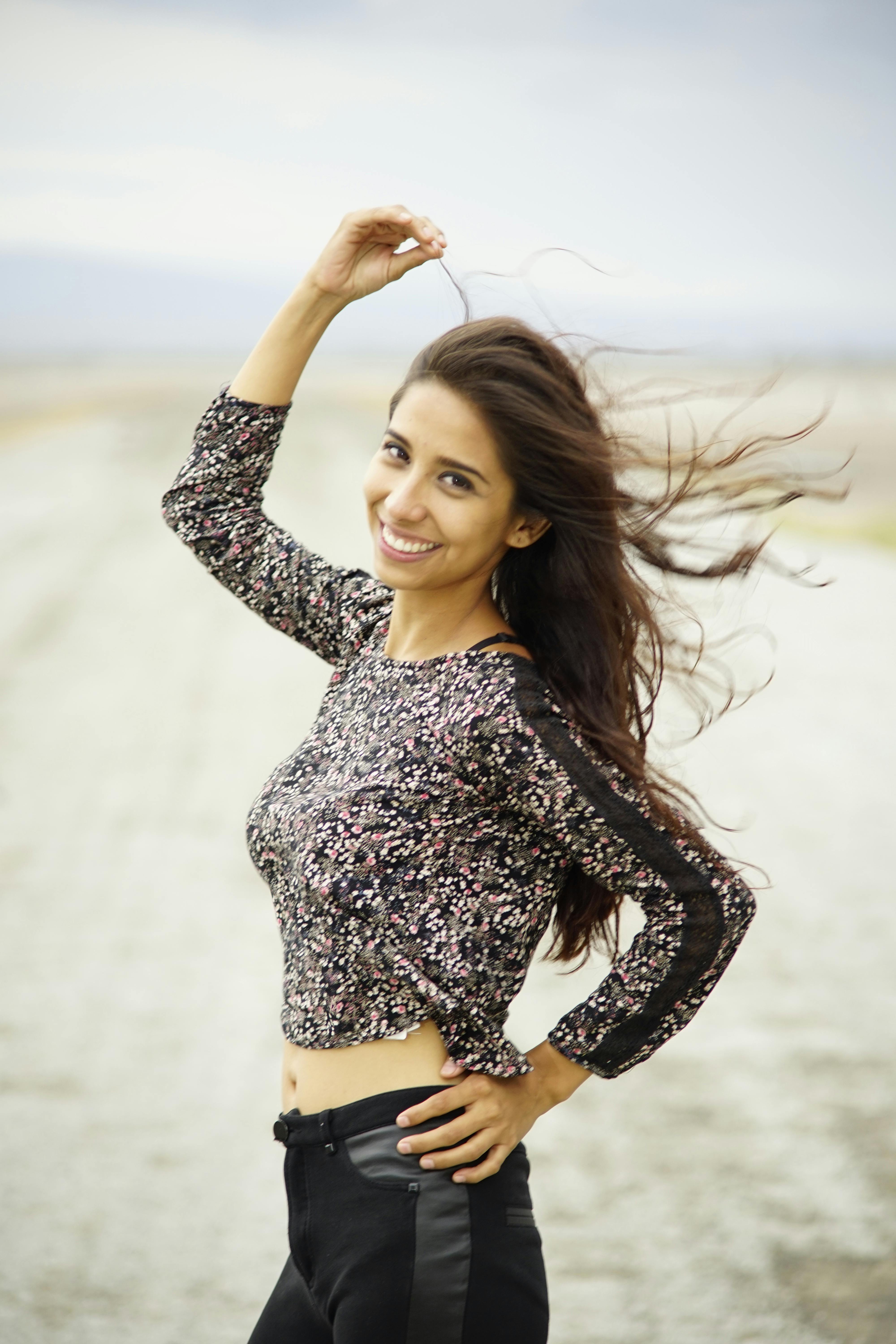 Smiling woman in a floral crop top enjoying a windy day outdoors.