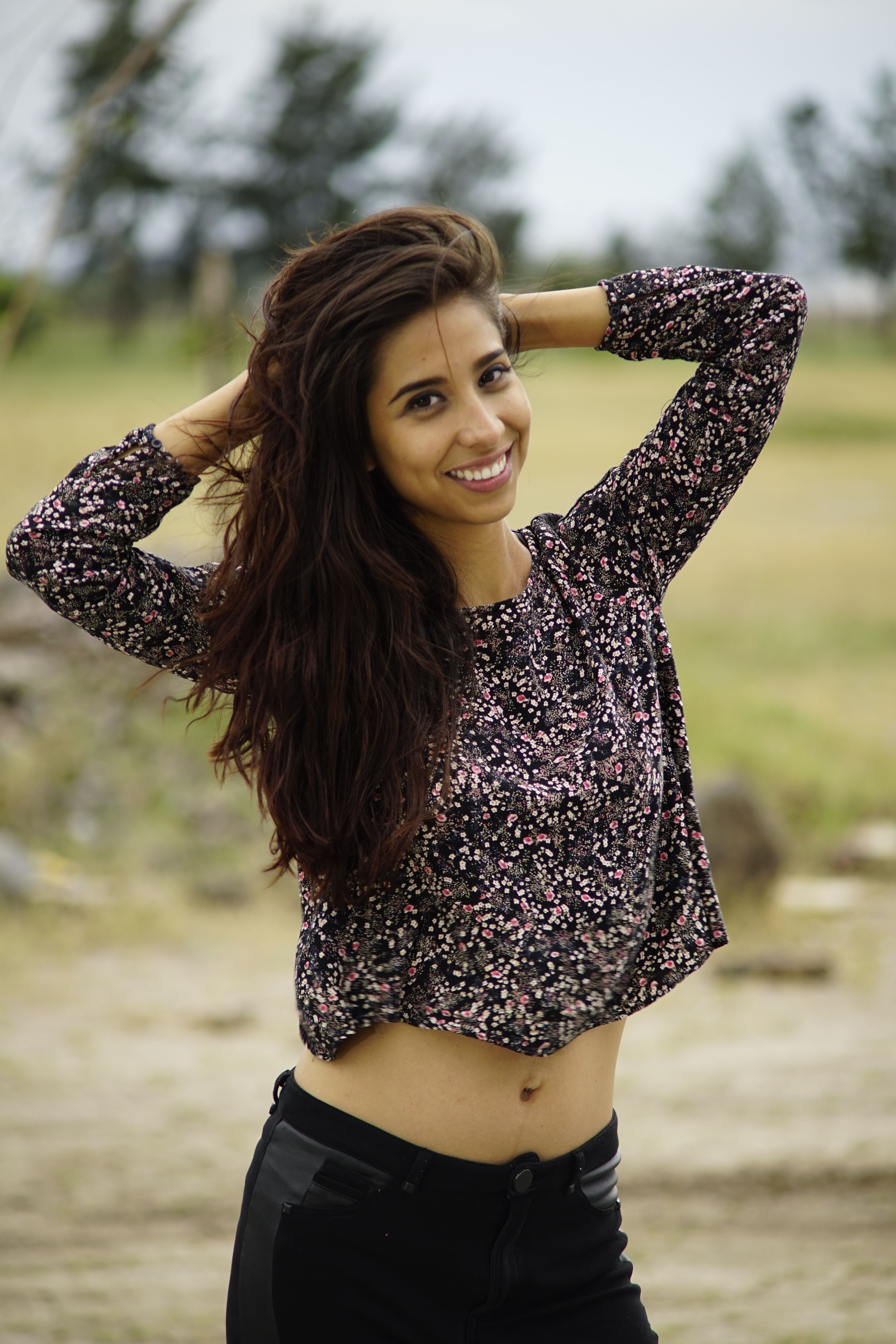 A happy young woman poses confidently outdoors in a floral top, exuding joy and confidence.