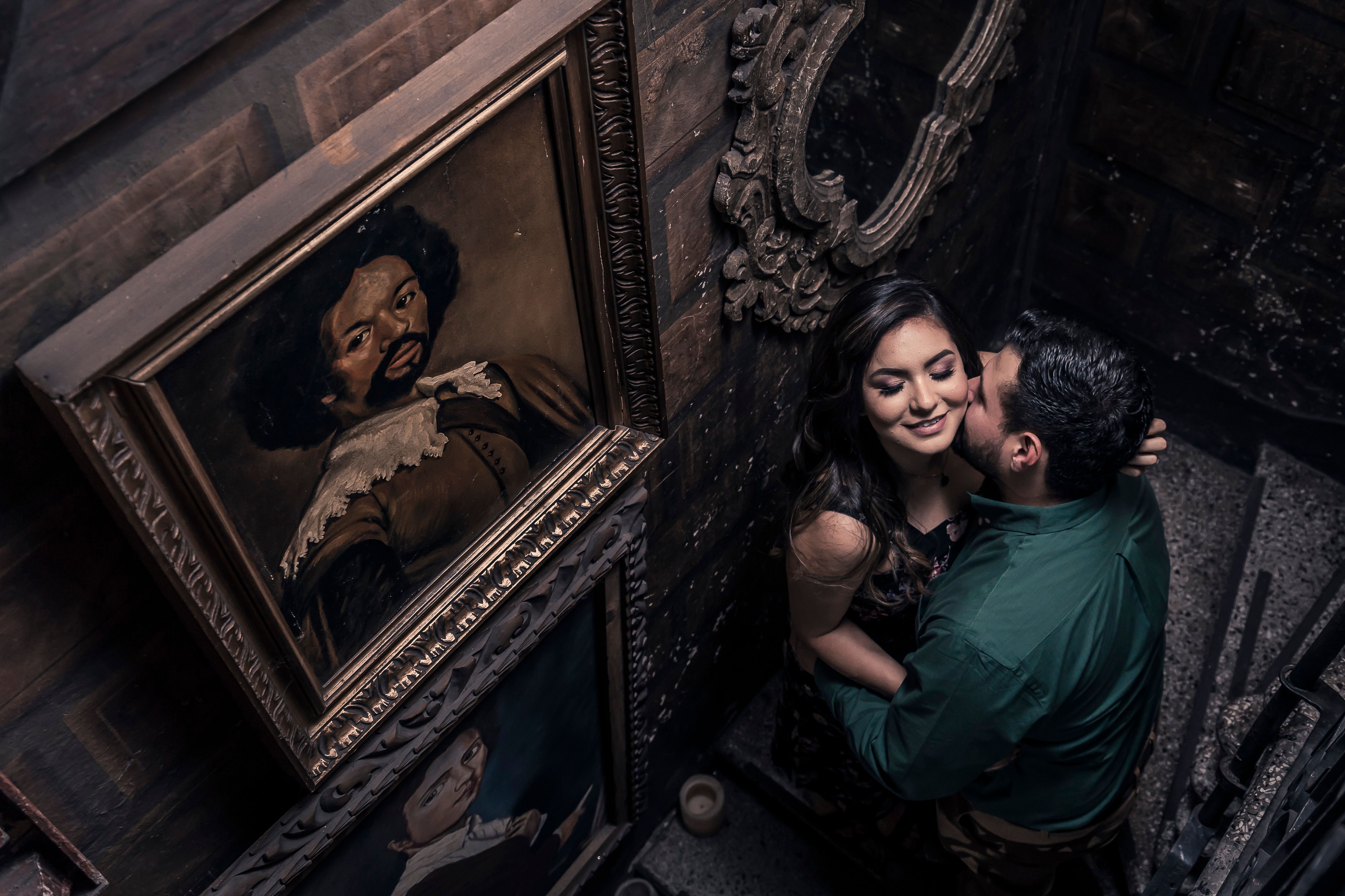 A loving couple shares an intimate moment on a vintage stairway, surrounded by classic portraits.