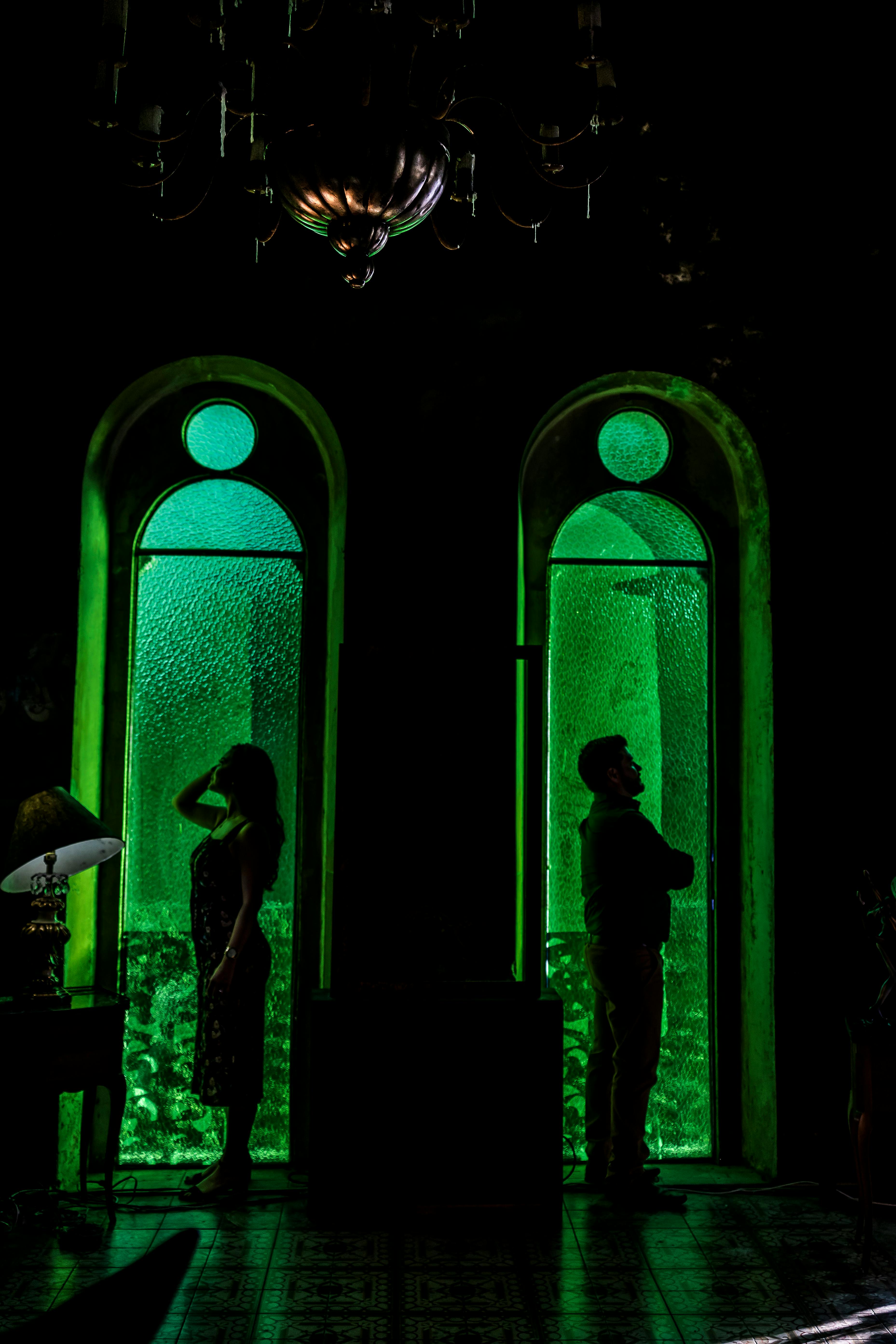 Free Silhouetted couple poses amid green-lit vintage windows, adding a romantic and artistic touch. Stock Photo