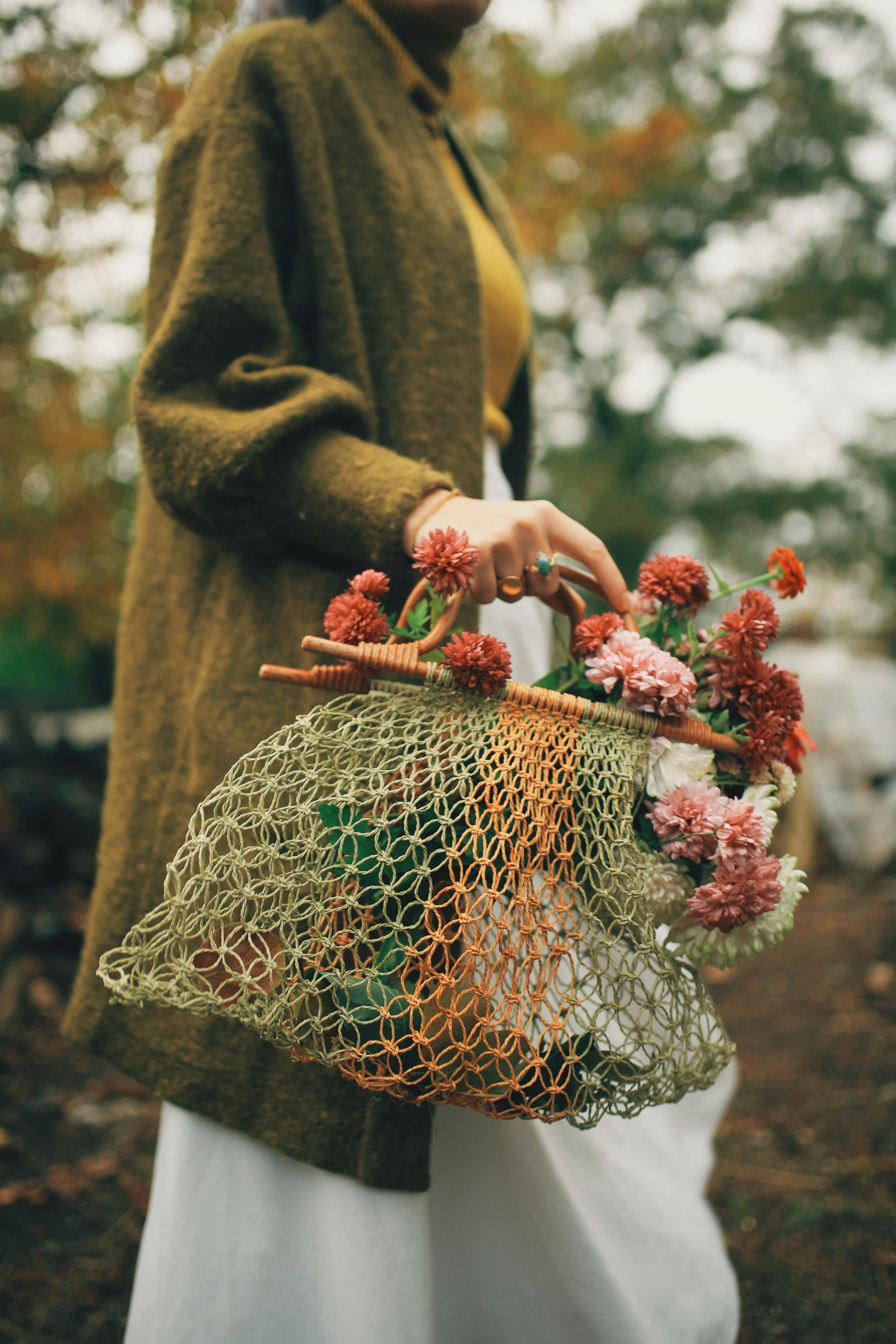 crop woman in warm outfit carrying knitted shopper with red flowers