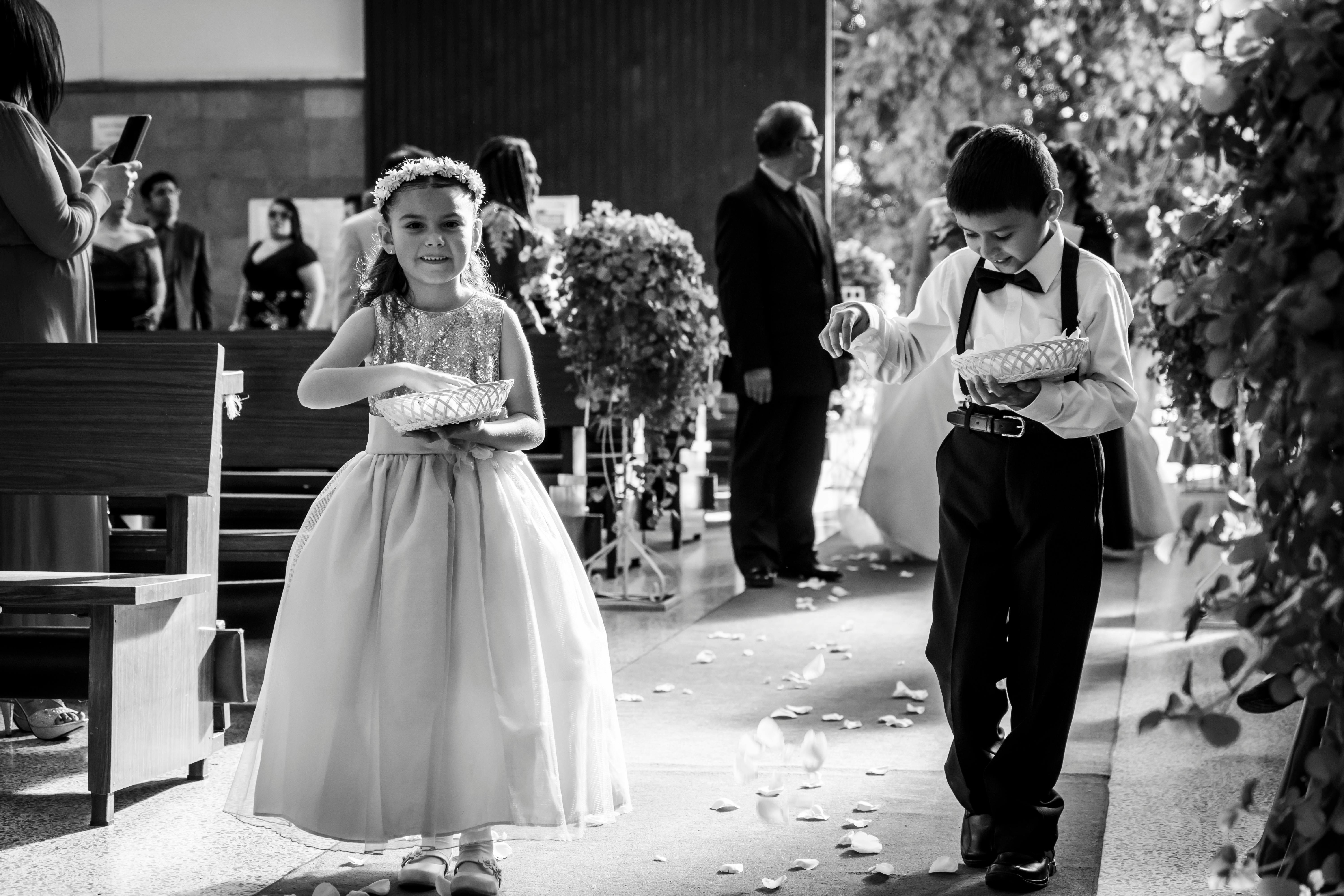 A delightful black and white capture of a flower girl and ring bearer walking down the aisle during a wedding.