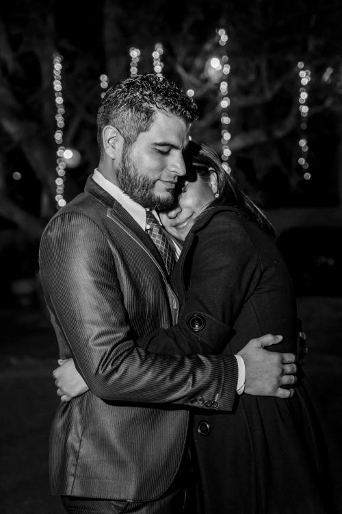 Free A couple lovingly hugging at night with decorative lights in the background. Stock Photo