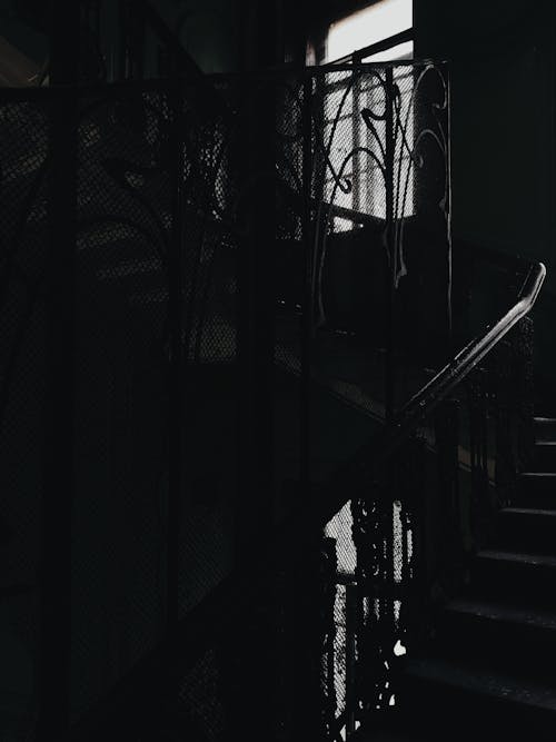 Black and White Photo of a Dark Interior with a Staircase and Vintage Handrail